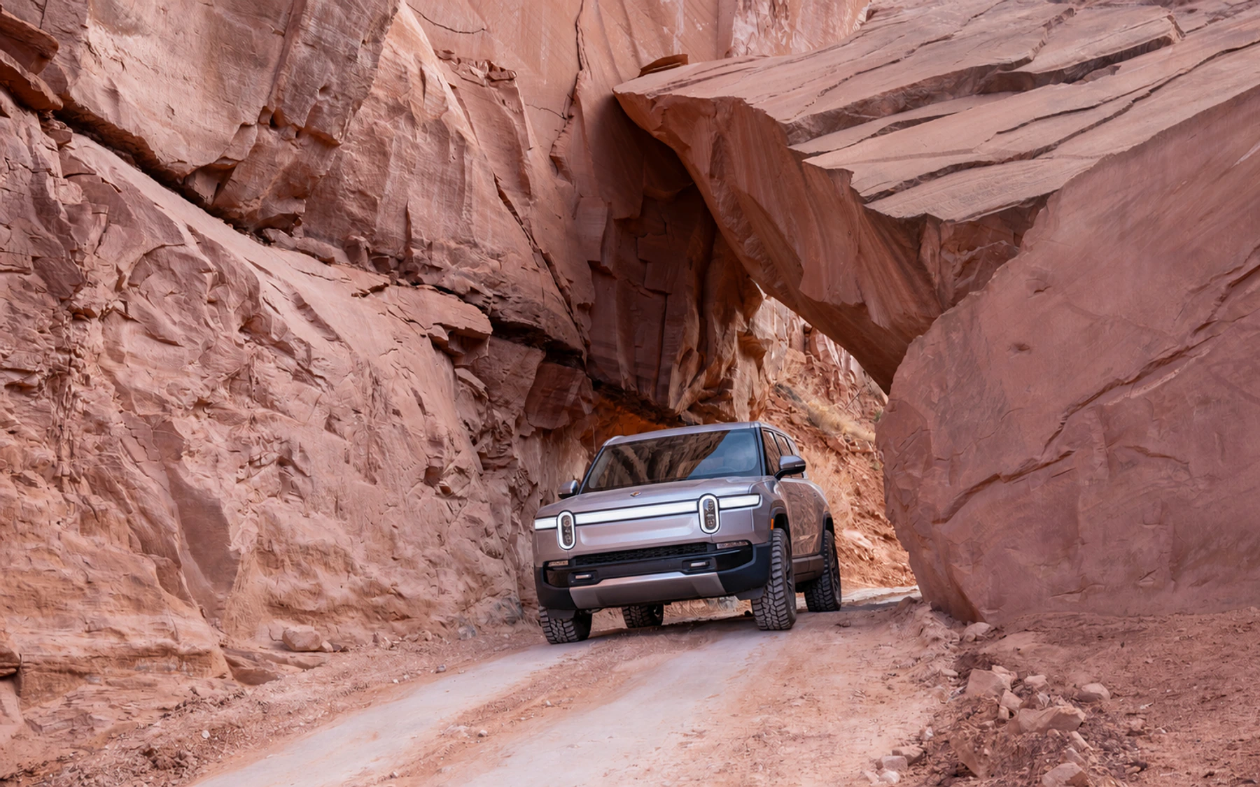 A silver Rivian R1S passing beneath the rock on Long Canyon Road