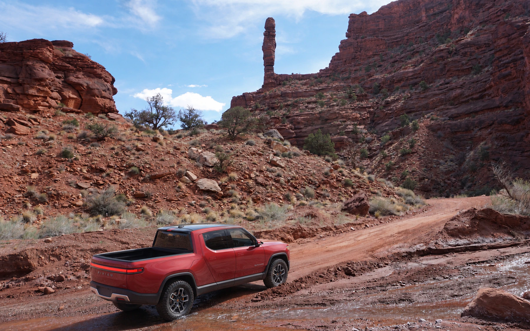 A red Rivian R1T crossing Onion Creek below the red canyon walls