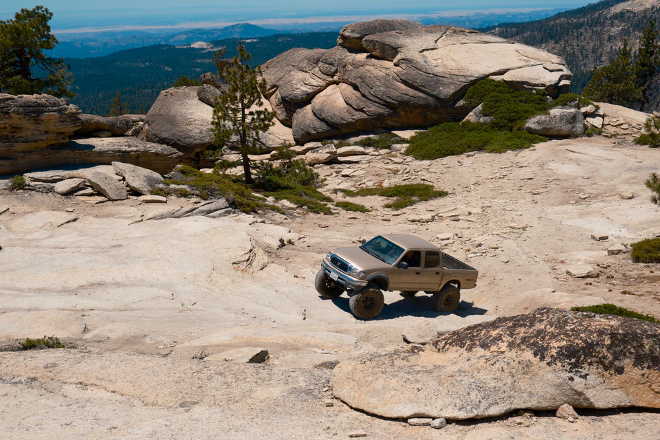 A pickup truck crossing pale granite slickrock near Shuteye Peak beneath scattered conifers.