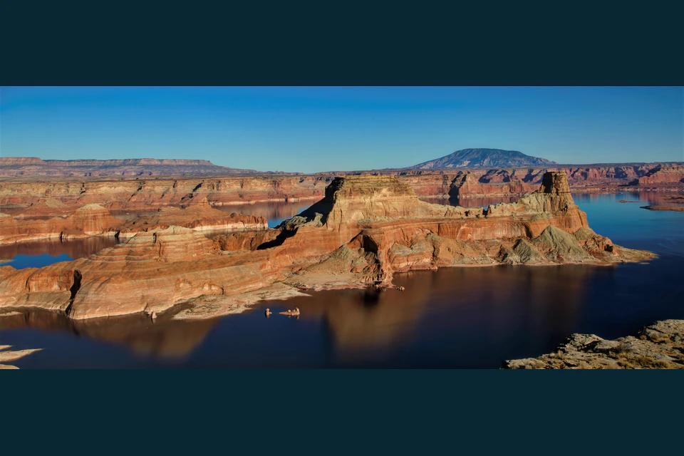 Gunsight Butte rising from Lake Powell, with sandstone mesas and Navajo Mountain in the distance.