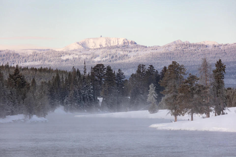 Snow-covered Sawtell Peak and its summit radar installation above forest and the Madison River.
