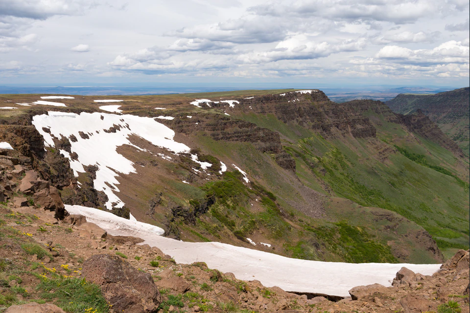 Snowbanks lining the Steens Mountain rim above the steep green slopes of Kiger Gorge.